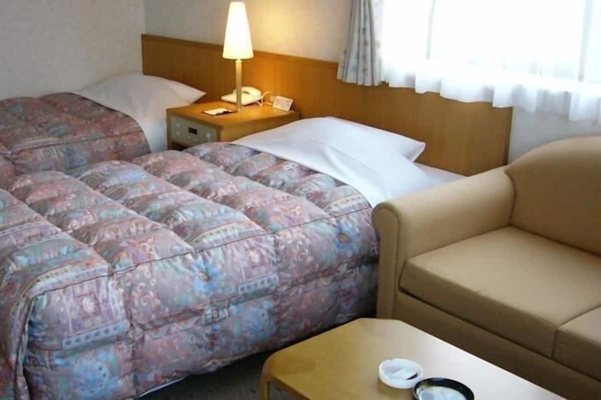 A hotel room with two beds, a nightstand with a lamp, a sofa, and a small table.