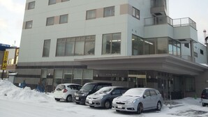 A multi-story building with a flat facade, large windows, and a parking area with several cars.
