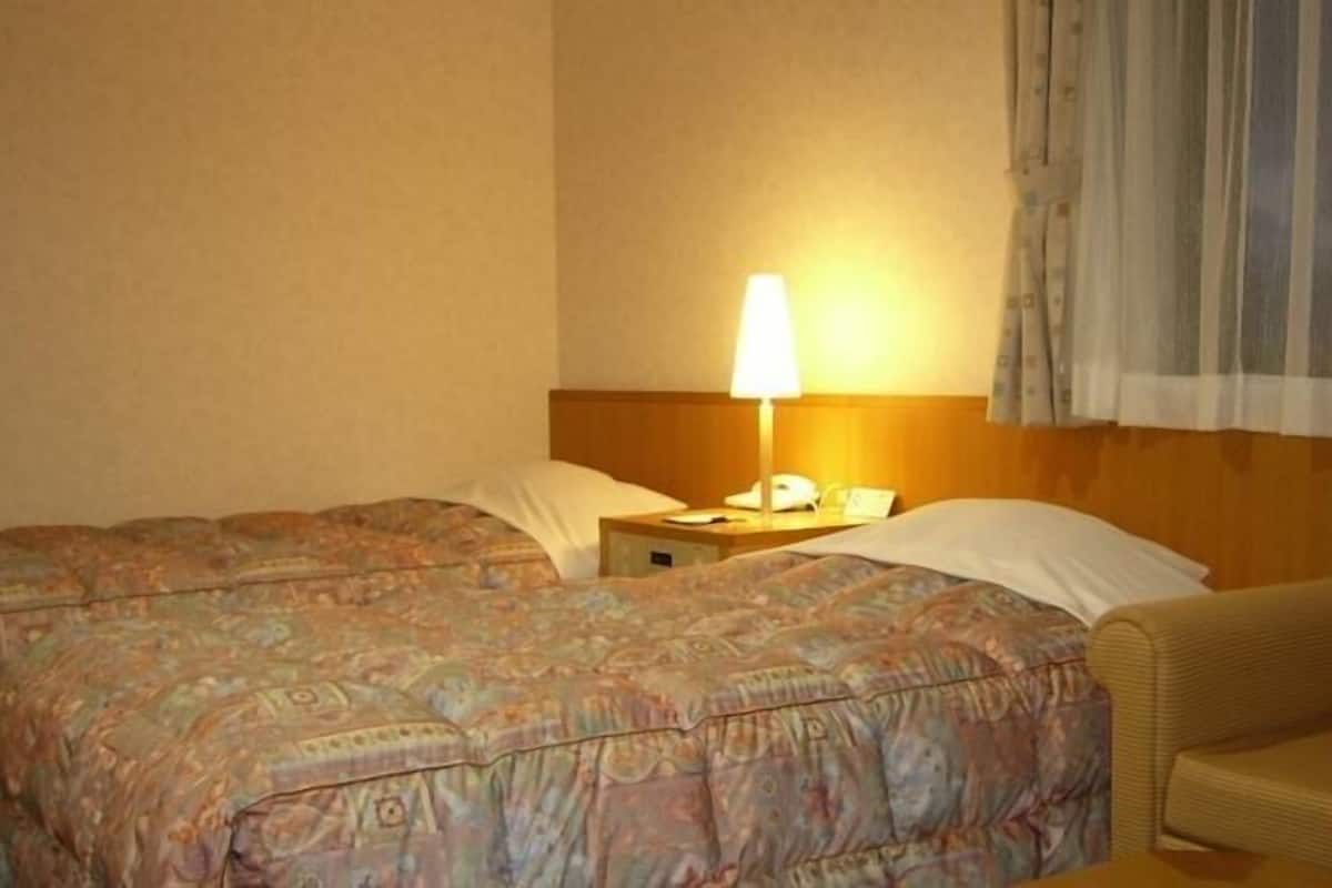 A hotel room with two beds, a bedside table with a lamp, and a chair.