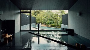 A modern bathroom with a glass-enclosed pool, a wooden bench, and a view of a lush garden. - Beniya (Awara)