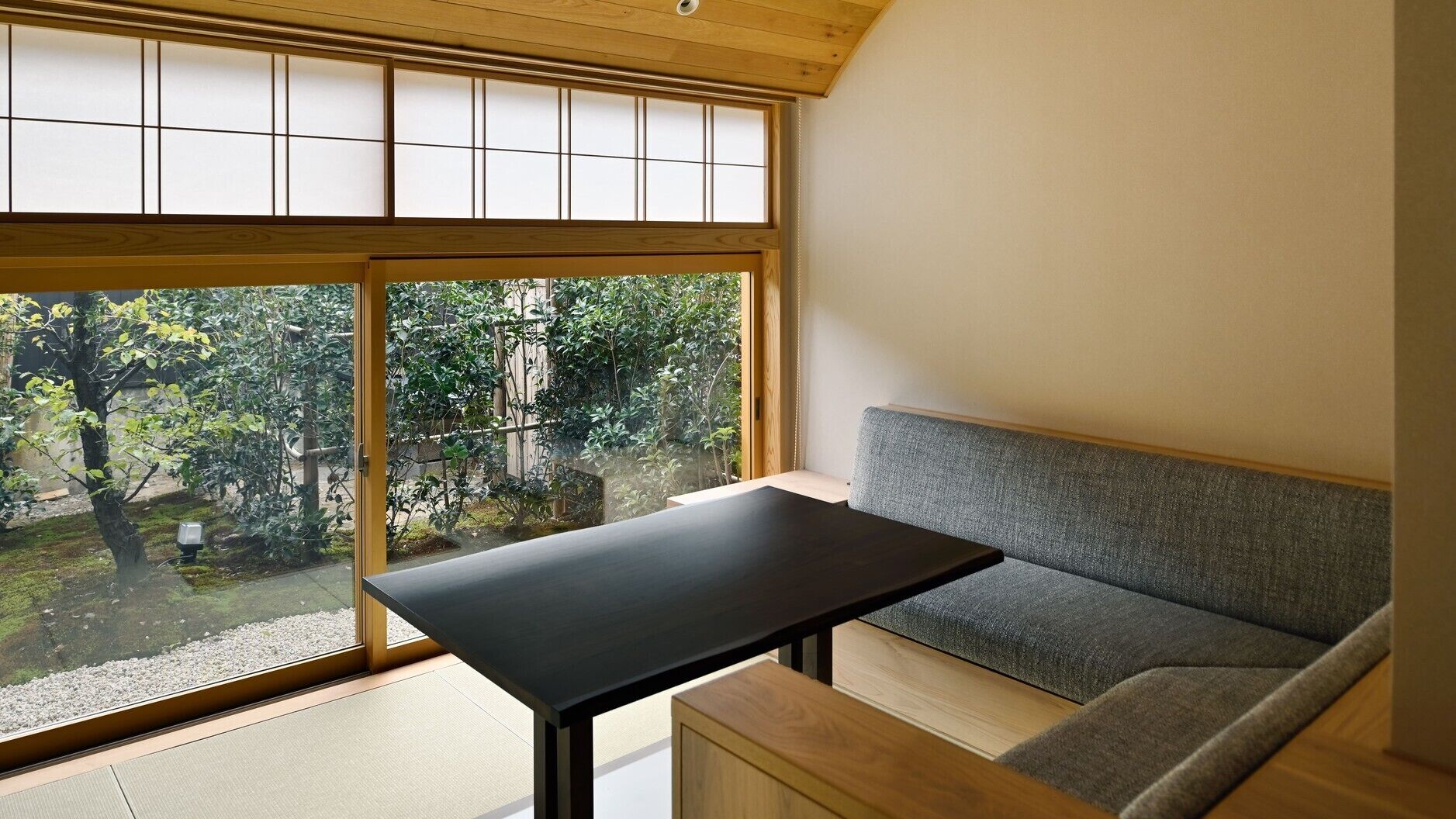 A room with a large window, a black table, and a grey sofa.