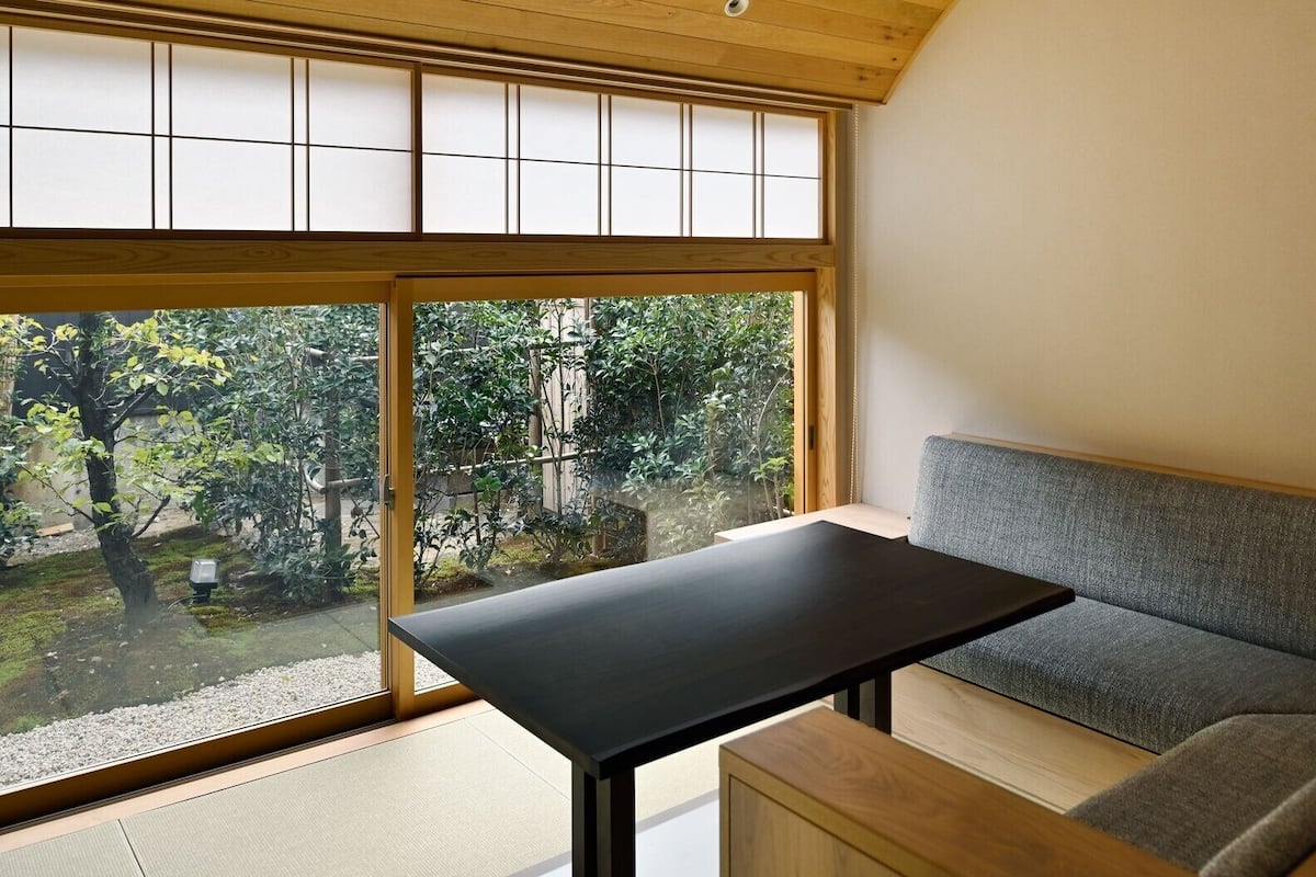 A room with a large window, a black table, and a grey sofa.