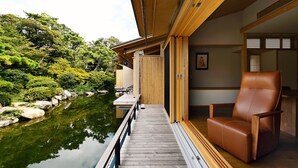 A wooden deck leading to a traditional Japanese room with tatami flooring and a view of a koi pond. - Beniya (Awara)