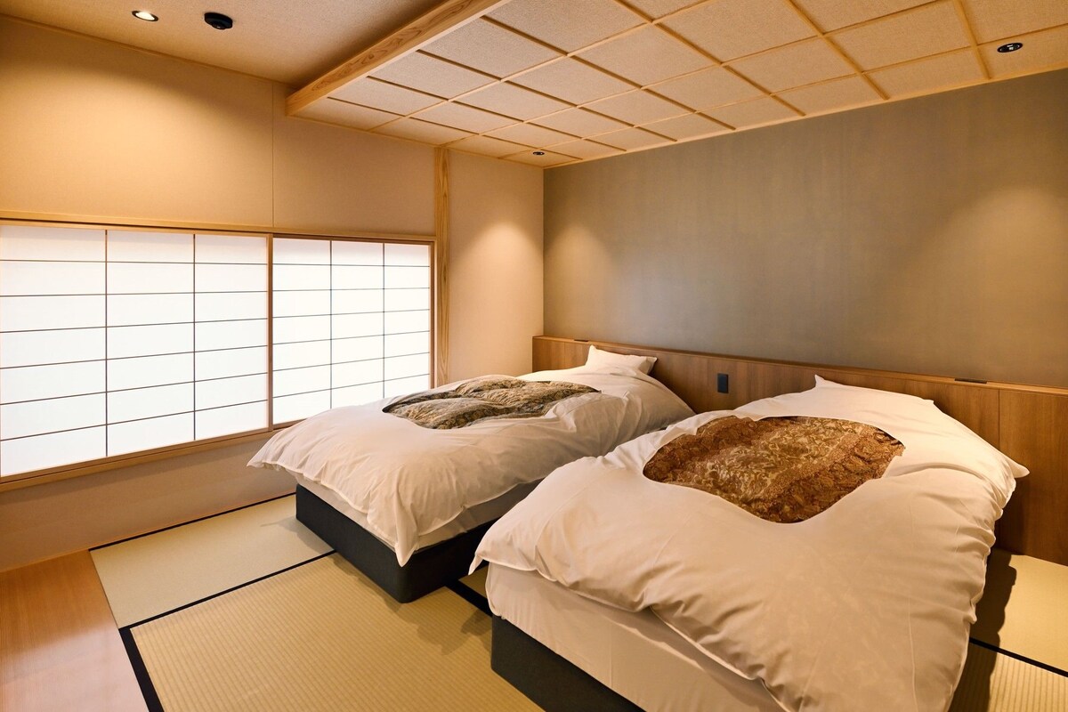 A traditional Japanese-style room with tatami flooring, two beds with headboards, and a shoji screen window.