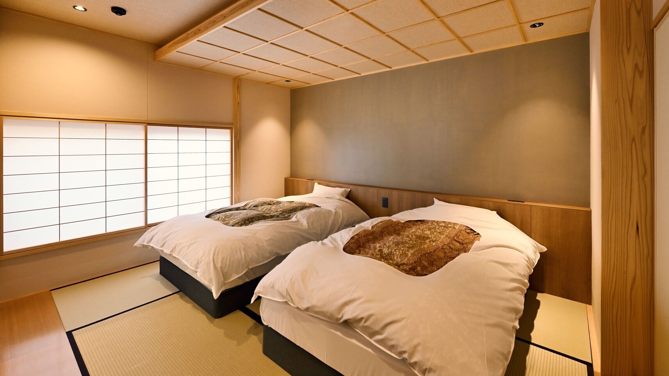 A traditional Japanese-style room with tatami flooring, two beds with headboards, and a shoji screen window.