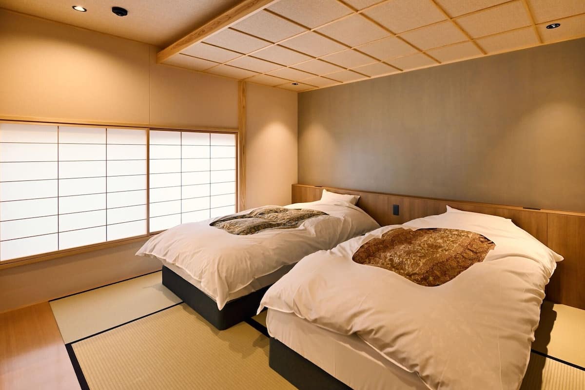A traditional Japanese-style room with tatami flooring, two beds with headboards, and a shoji screen window.