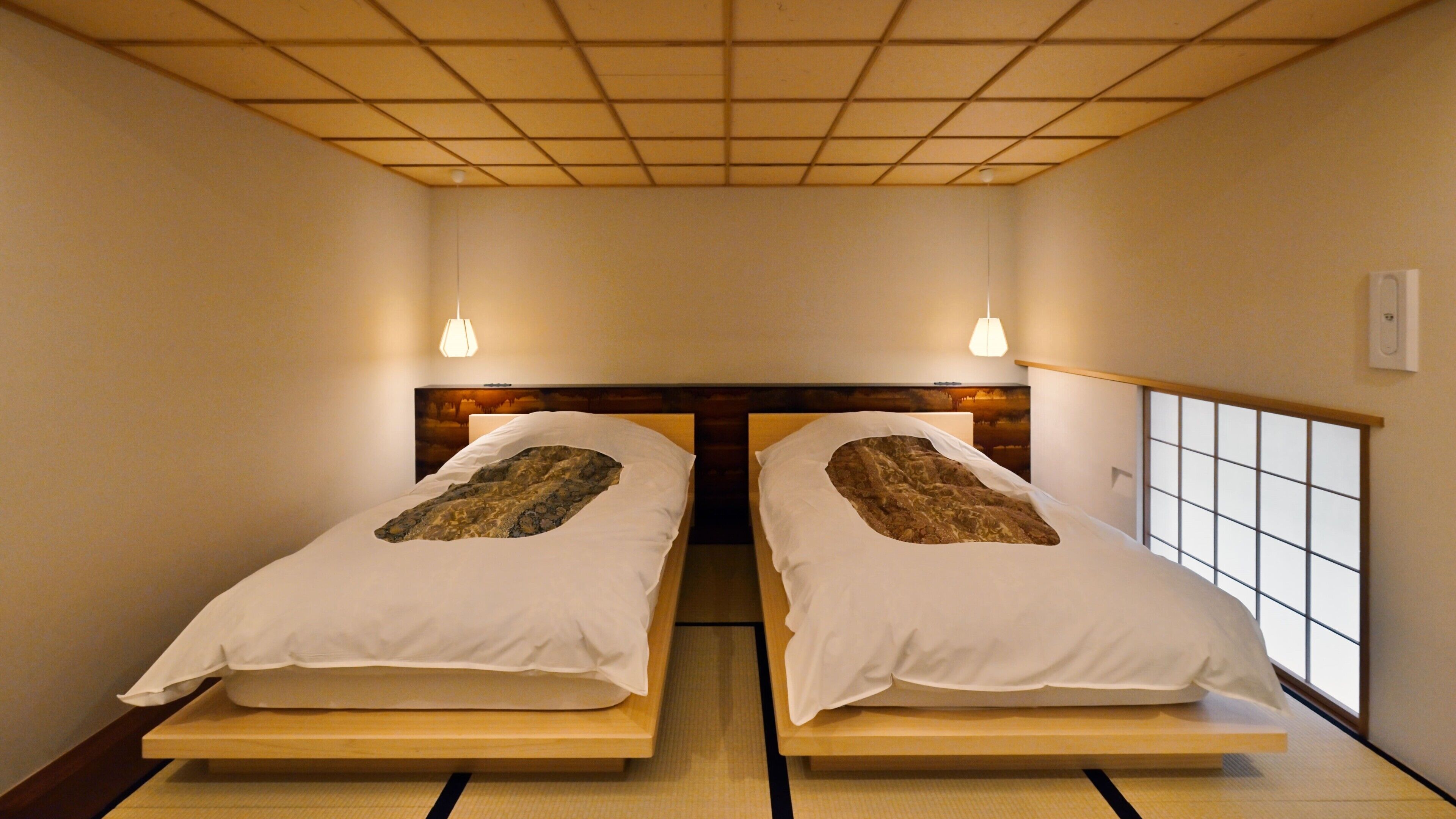 A room with two beds, a wooden headboard, a tatami mat floor, and a window with a grid pattern.