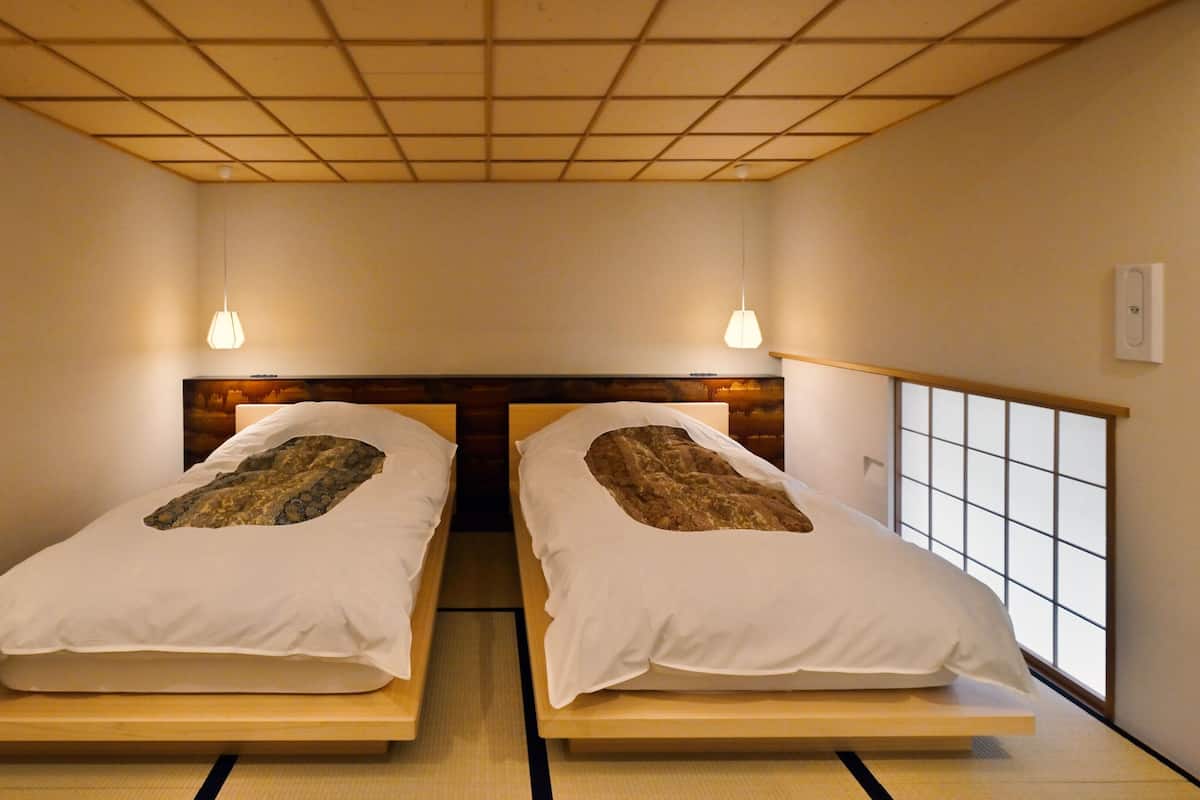 A room with two beds, a wooden headboard, a tatami mat floor, and a window with a grid pattern.