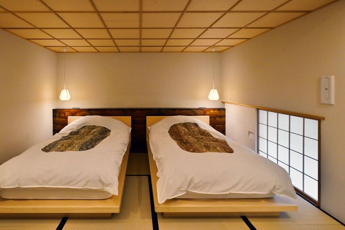 A room with two beds, a wooden headboard, a tatami mat floor, and a window with a grid pattern.