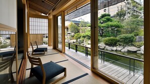 A traditional Japanese room with tatami flooring, a low wooden table, and a view of a garden through large sliding doors. - Beniya (Awara)