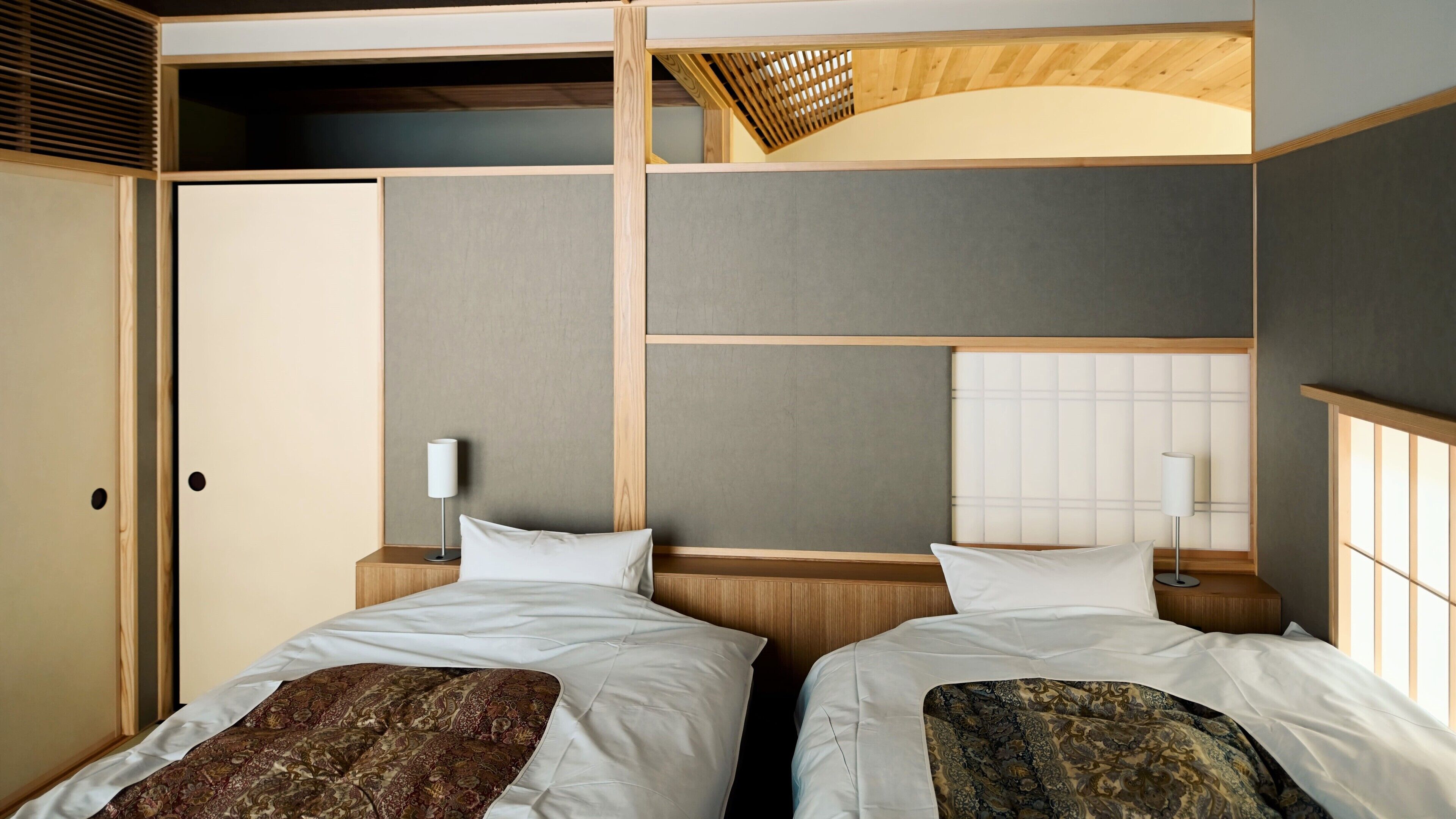 A hotel room with two beds, a wooden ceiling, and a view of the outside.