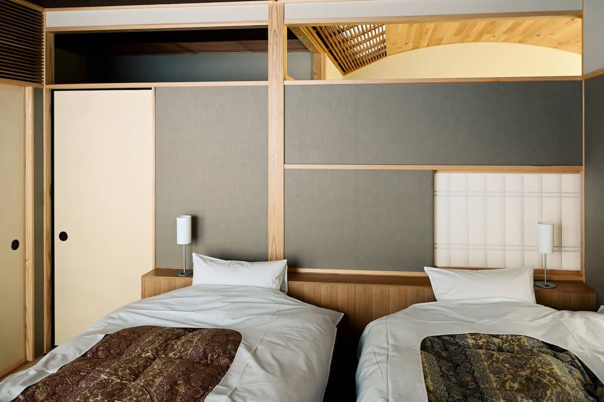 A hotel room with two beds, a wooden ceiling, and a view of the outside.