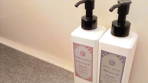 Two white bottles with black pumps, labeled 'RINSE SHAMPOO' and 'BODY SOAP,' placed against a wall. - Matsue Plaza Hotel Annex (Matsue)