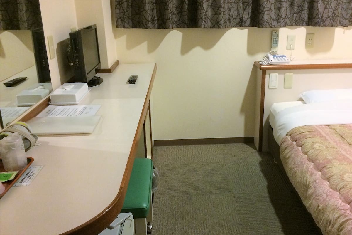 Una habitación de hotel con escritorio, silla, cama, mesita de noche y teléfono.