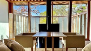 Een moderne eetruimte met een houten tafel en stoelen, grote ramen met uitzicht op bomen, en een plafond met houten latten.