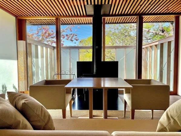 Un comedor moderno con una mesa y sillas de madera, ventanas amplias con vistas a árboles y un techo con listones de madera.