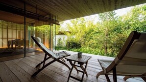 Een houten terras met twee ligstoelen en een kleine tafel, met uitzicht op een weelderige tuin.