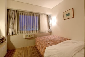 Een hotelkamer met een bed, een raam met gordijnen, een nachtkastje en een aan de muur hangend schilderij.