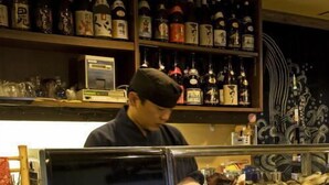 A person behind a counter with shelves of bottles and a display case with food items. - Takamatsu Hotel Sakika (Takamatsu)