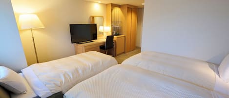 A hotel room with two beds, a desk with a TV, a lamp, and a wardrobe.