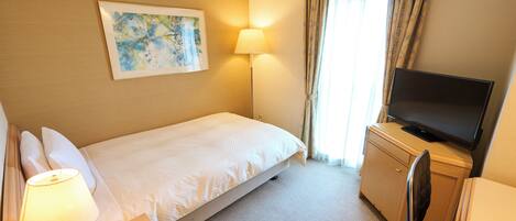 Quarto de hotel com cama, escrivaninha, televisão, candeeiro e um quadro na parede.