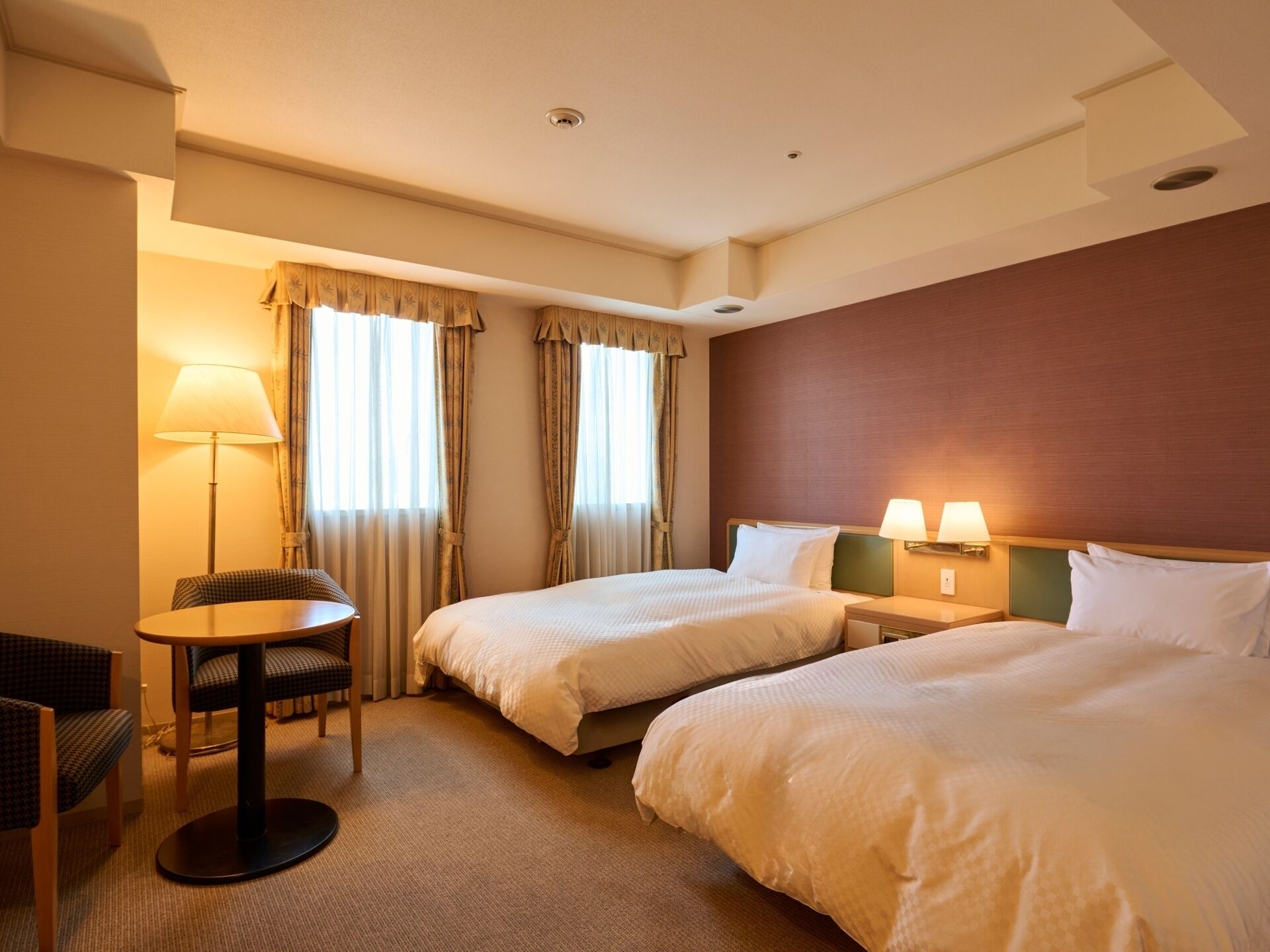 A hotel room with two beds, a desk, and a chair.