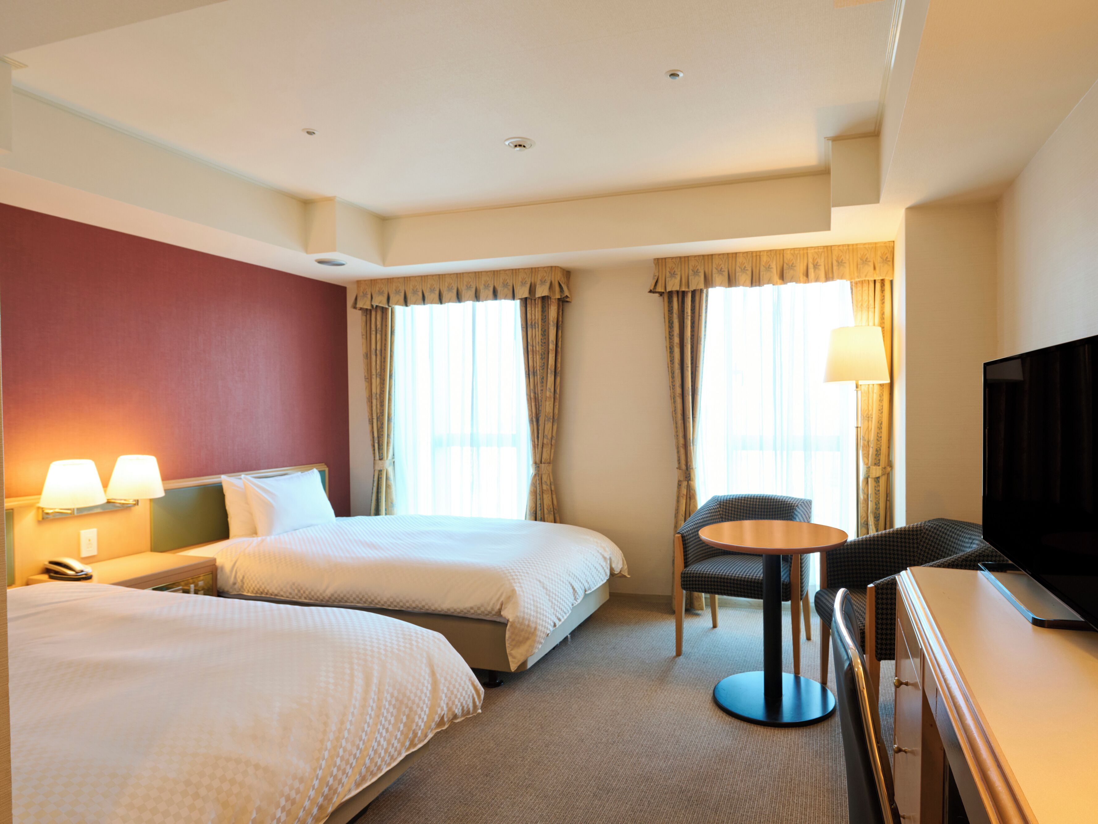 Een hotelkamer met twee bedden, een bureau, een stoel, een televisie en twee lampen.