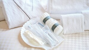 Un conjunto ordenado de artículos de aseo que incluye un cepillo de dientes, pasta dental y un exfoliante corporal sobre una bandeja blanca, con toallas dobladas al fondo.