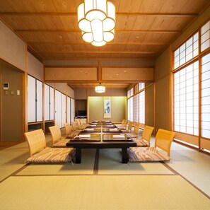 Une salle de réunion japonaise traditionnelle, avec un sol recouvert de tatamis, une longue table et des portes coulissantes.