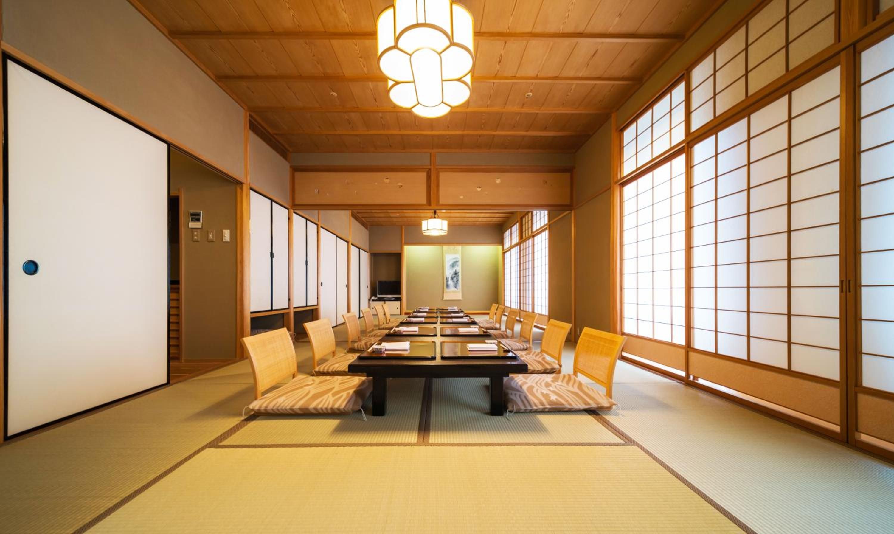 A traditional Japanese-style room with tatami flooring, a low table with cushions, sliding doors, and a hanging light fixture.