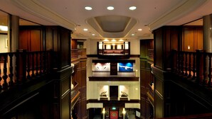 Un'imponente hall d'hotel con una scalinata centrale, ringhiere elaborate e un soffitto decorativo.