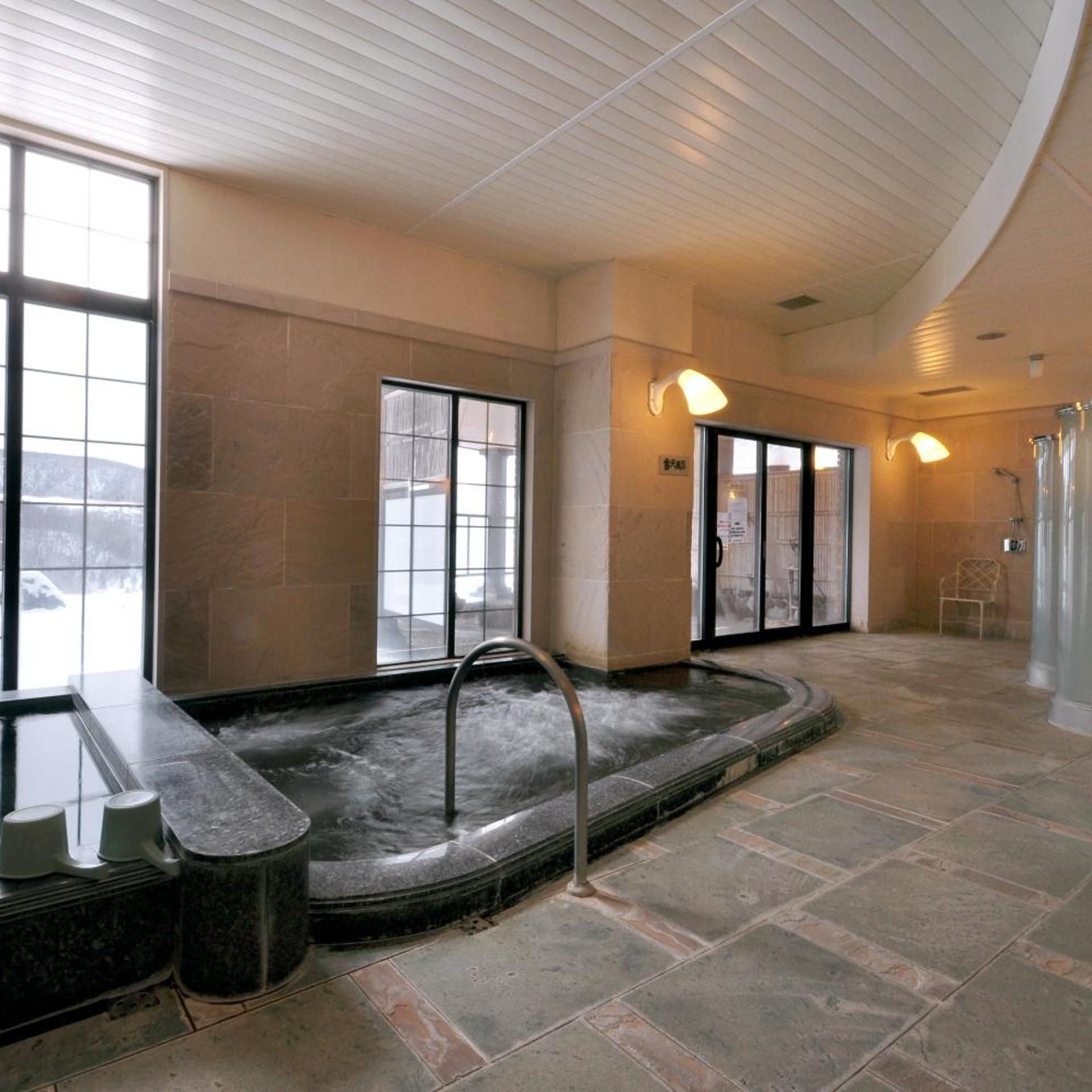 Zona de spa con hidromasaje, suelo de piedra y amplios ventanales.