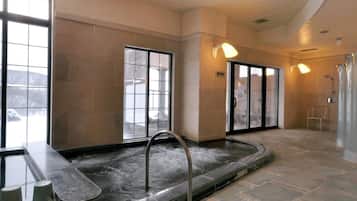 Zona de spa con hidromasaje, suelo de piedra y amplios ventanales.