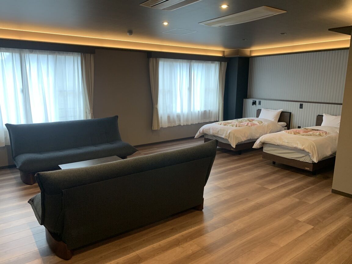 Habitación de hotel con sofá, dos camas y un ventanal con cortinas.