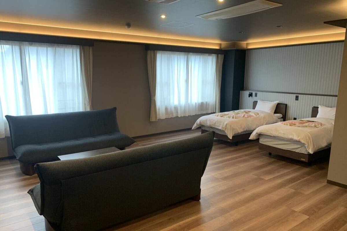Une chambre d’hôtel avec un canapé, deux lits et une grande fenêtre avec des rideaux.
