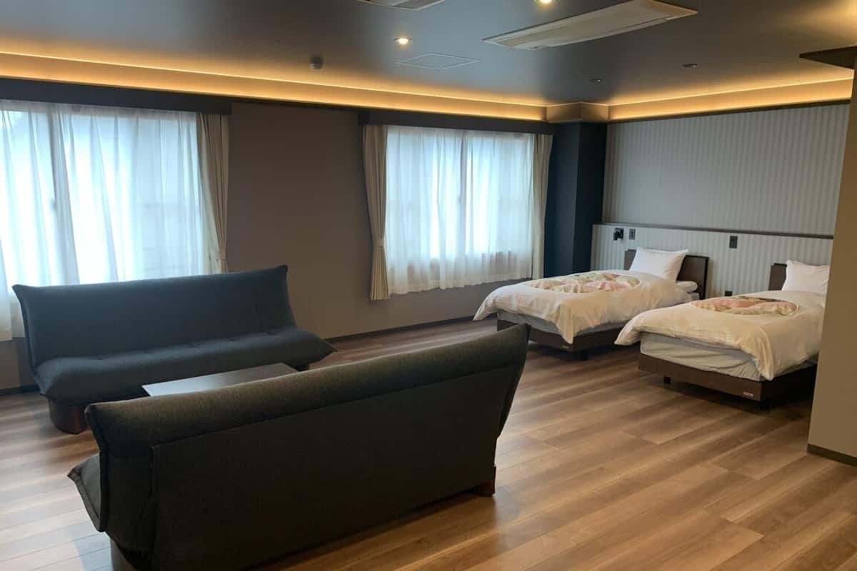 Ein Hotelzimmer mit einer Couch, zwei Betten und einem großen Fenster mit Vorhängen.