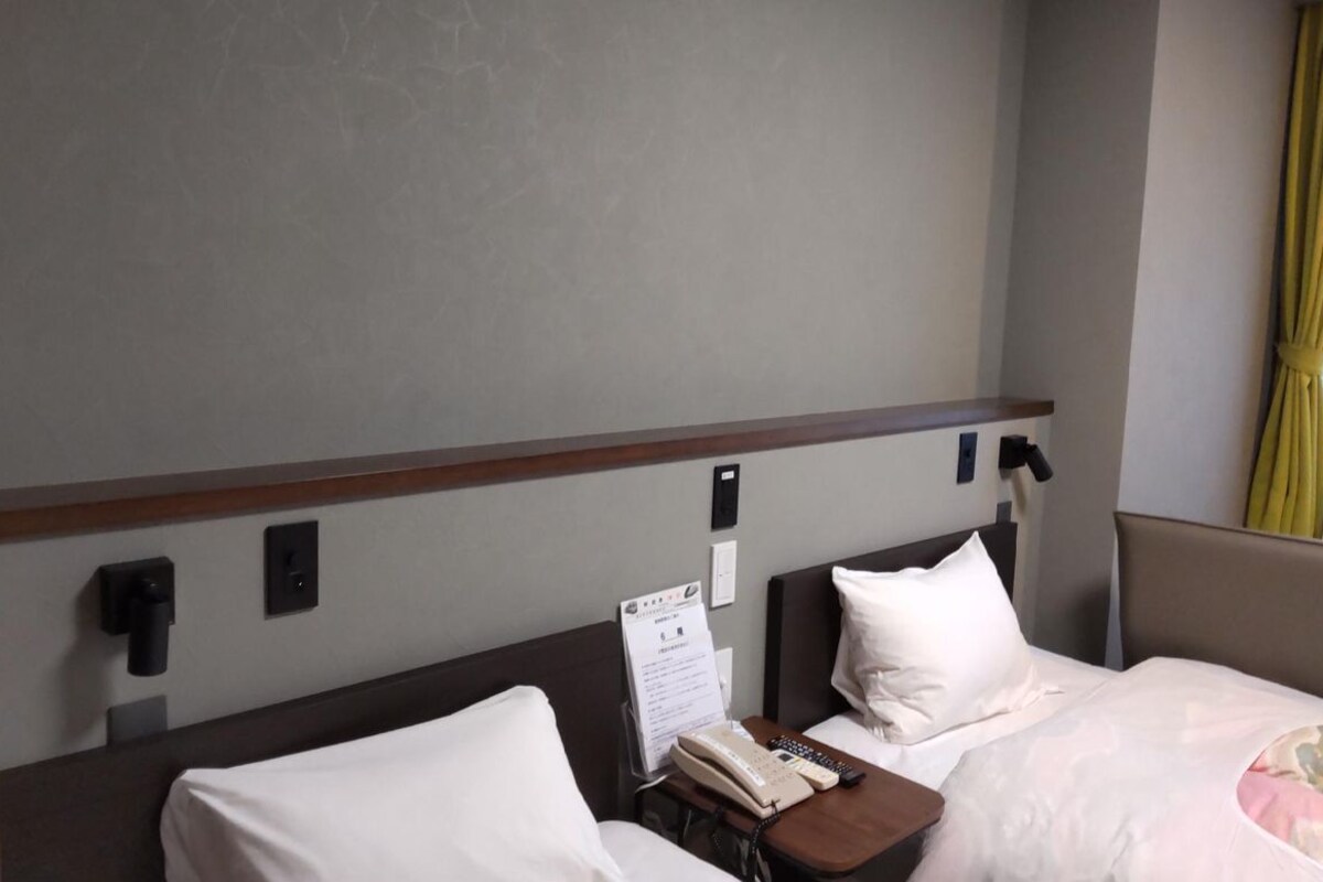 Een hotelkamer met een bed, nachtkastje en een telefoon aan de muur.