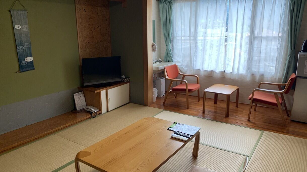 Una habitación con esteras de tatami, televisor, escritorio, silla y refrigerador.