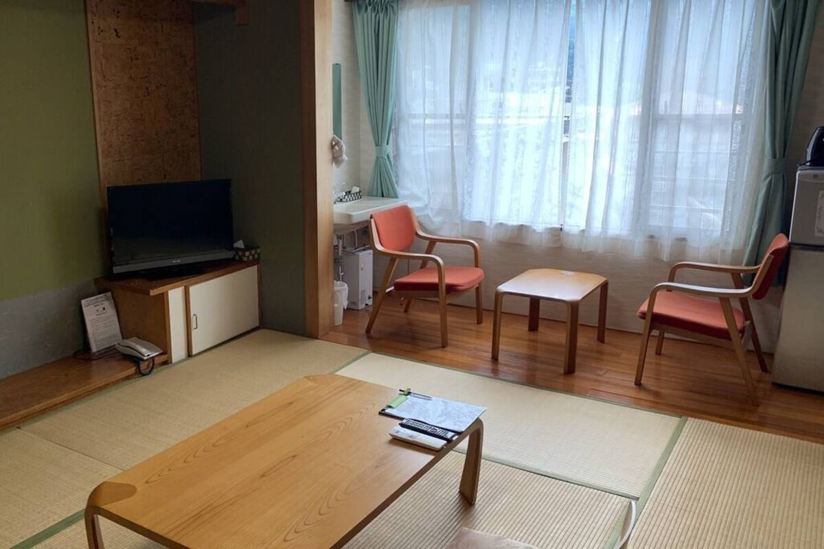 Une pièce avec des tatamis, une télévision, un bureau, une chaise et un réfrigérateur.