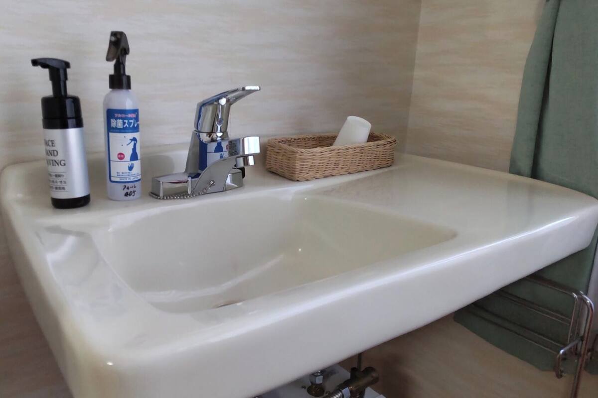 Un lavabo de salle de bain avec un flacon de savon liquide, un flacon de lotion et un petit panier contenant des mouchoirs.