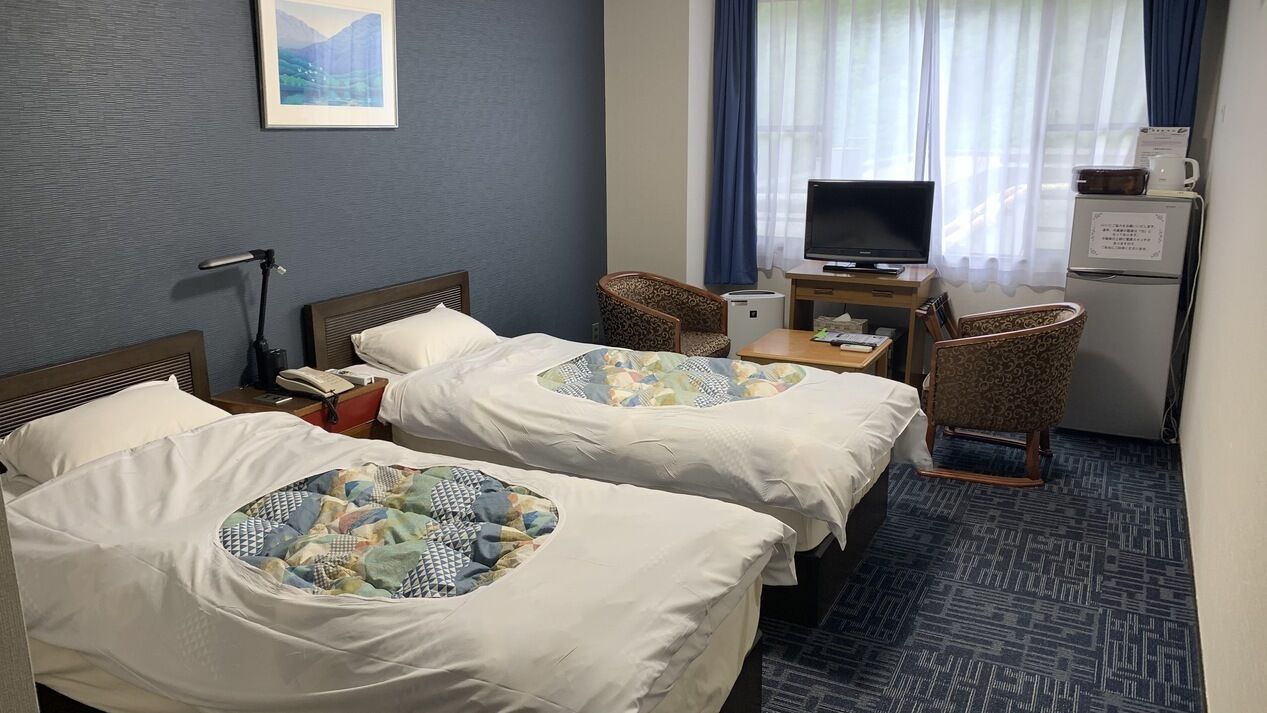 Habitación de hotel con dos camas, un escritorio con computadora, una silla, un televisor y un refrigerador.