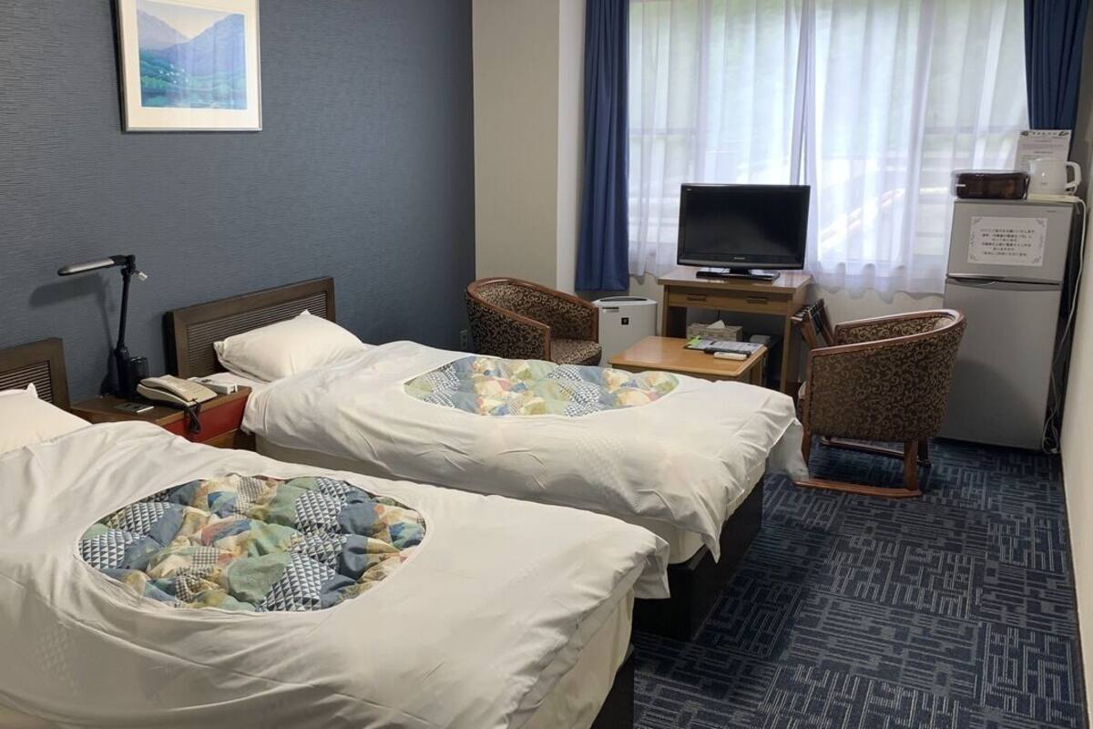 Une chambre d’hôtel avec deux lits, un bureau avec un ordinateur, une chaise, une télévision et un réfrigérateur.