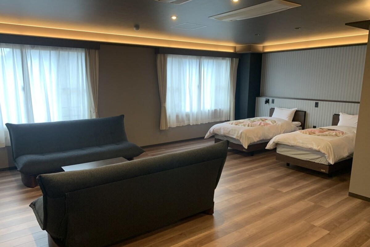 A hotel room with a sofa, two beds, and a large window with curtains.