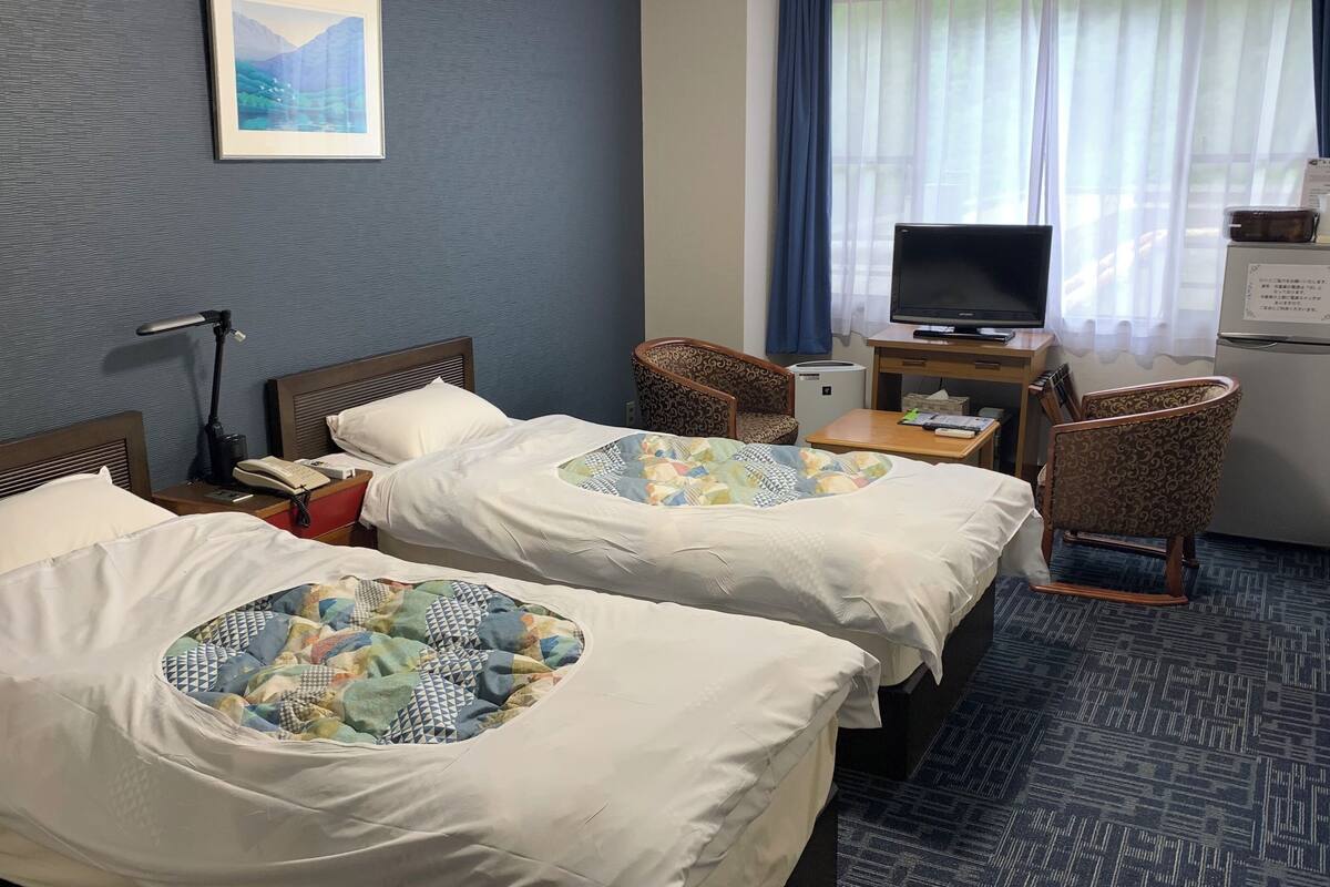 Une chambre d’hôtel avec deux lits, un bureau avec une télévision, une chaise et un petit réfrigérateur.