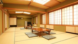 A traditional Japanese-style room with tatami flooring, a low table, cushions, sliding doors, and a television.