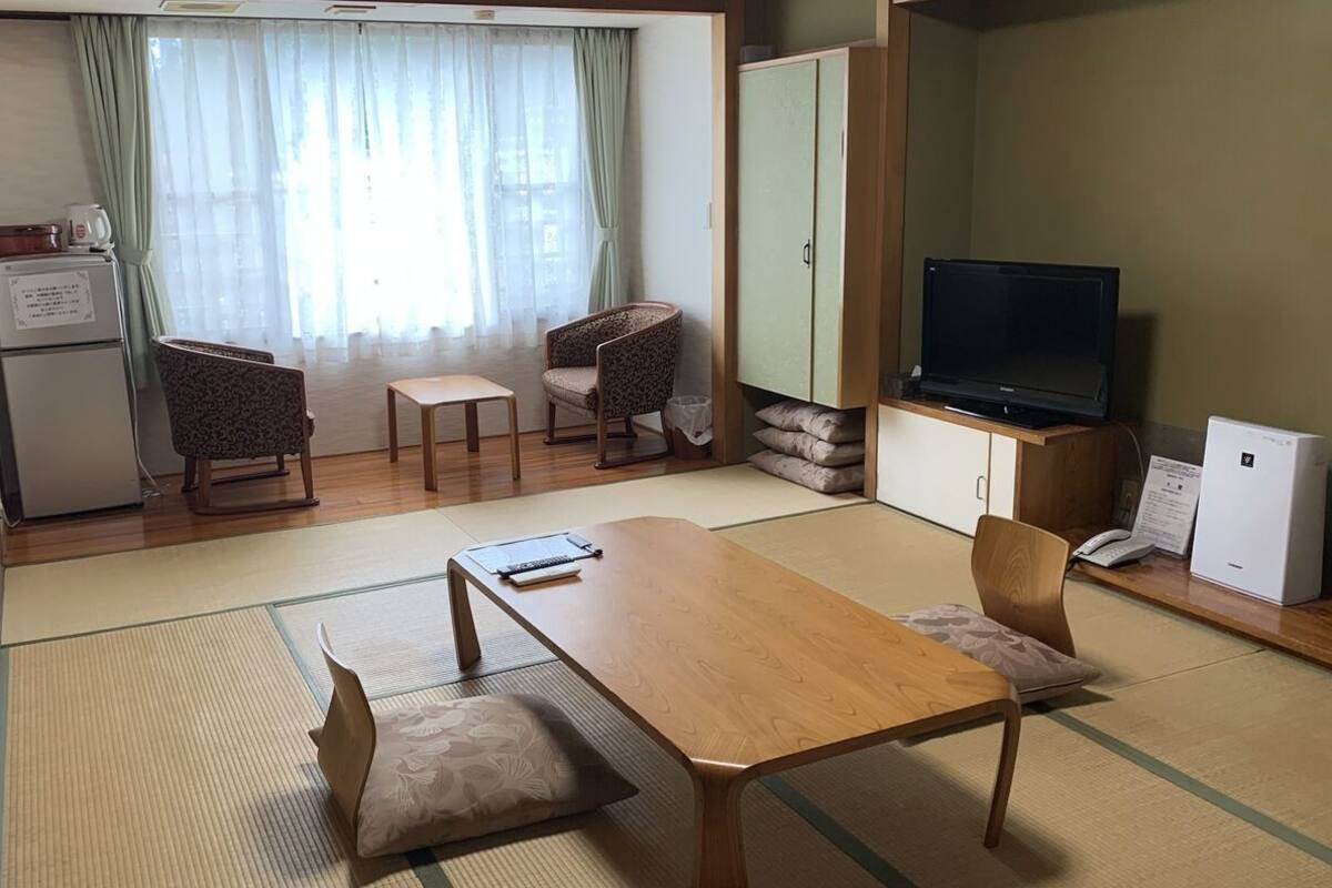 Un espace de vie compact comprenant une table à manger en bois, deux chaises, un téléviseur, un meuble et un réfrigérateur.