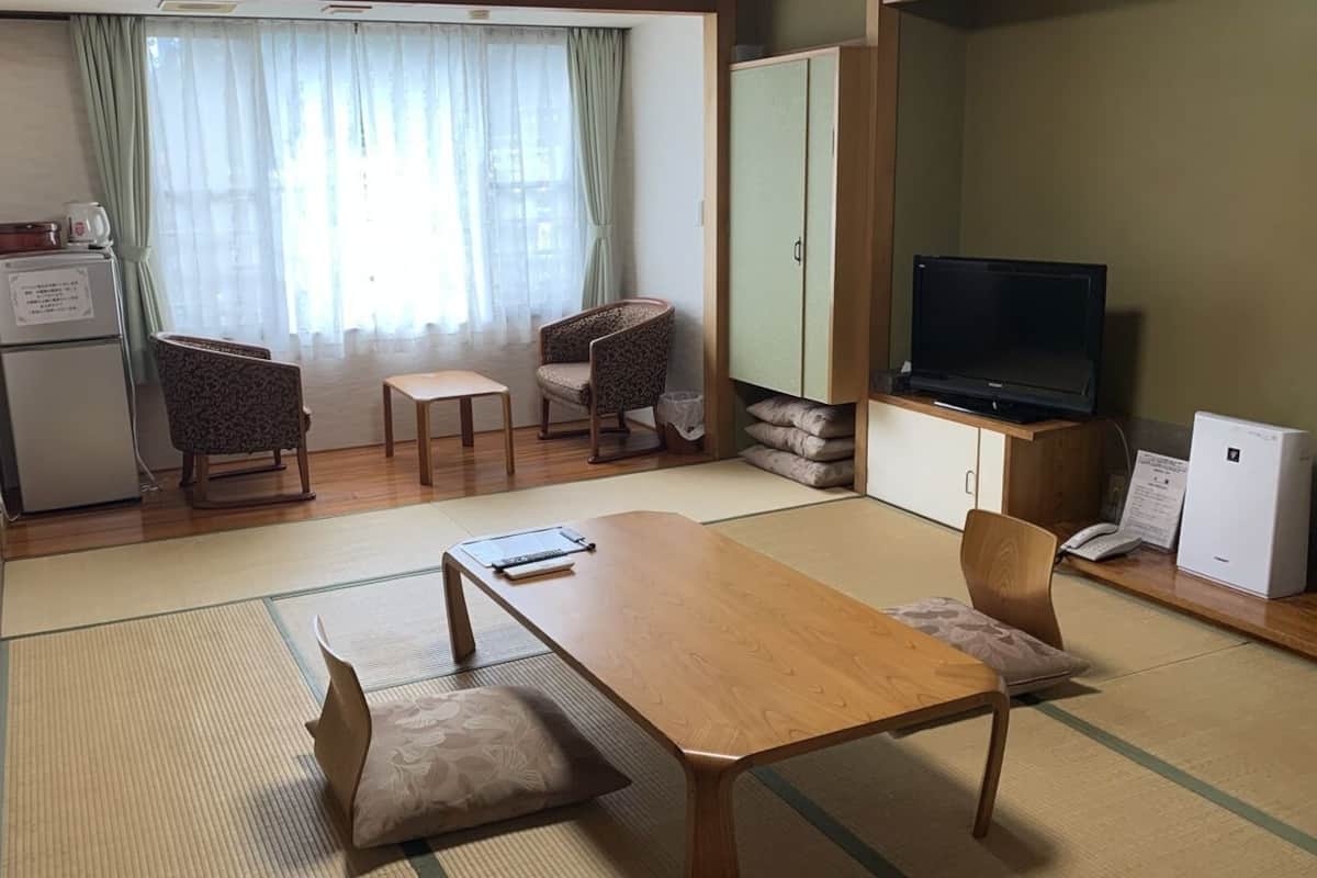 Ein kompakter Wohnraum mit Esstisch aus Holz, zwei Stühlen, einem Fernseher, einem Schrank und einem Kühlschrank.