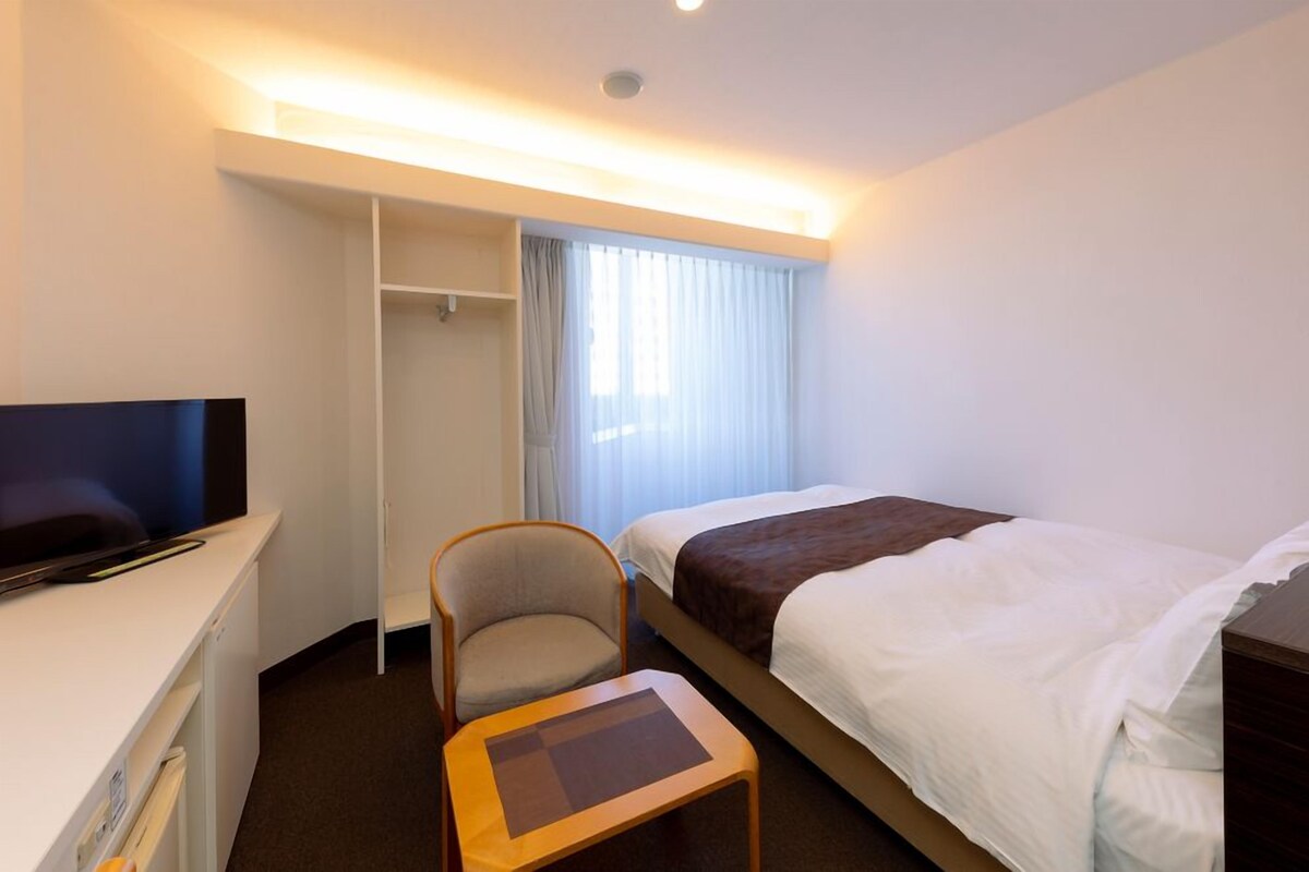 Ein Hotelzimmer mit Bett, Fernseher, Stuhl, Schreibtisch und Kleiderschrank.