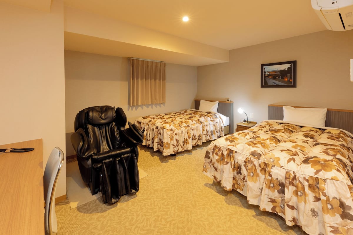 Habitació d'hotel amb dos llits, una butaca de cuir, un escriptori i una tauleta de nit.