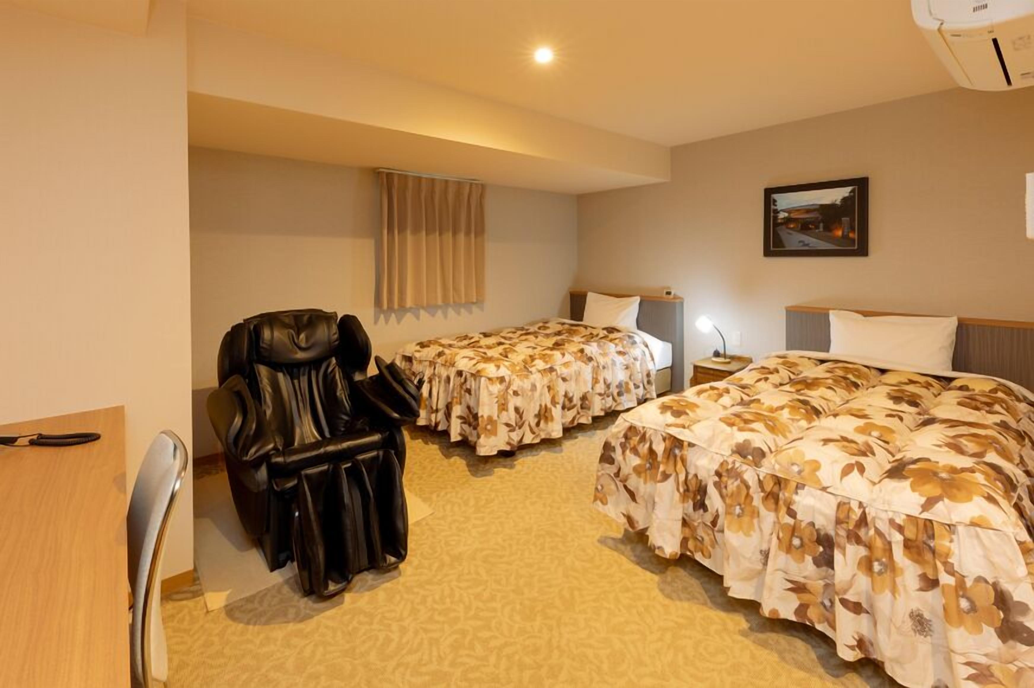 A hotel room with two beds, a leather chair, a desk, and a nightstand.
